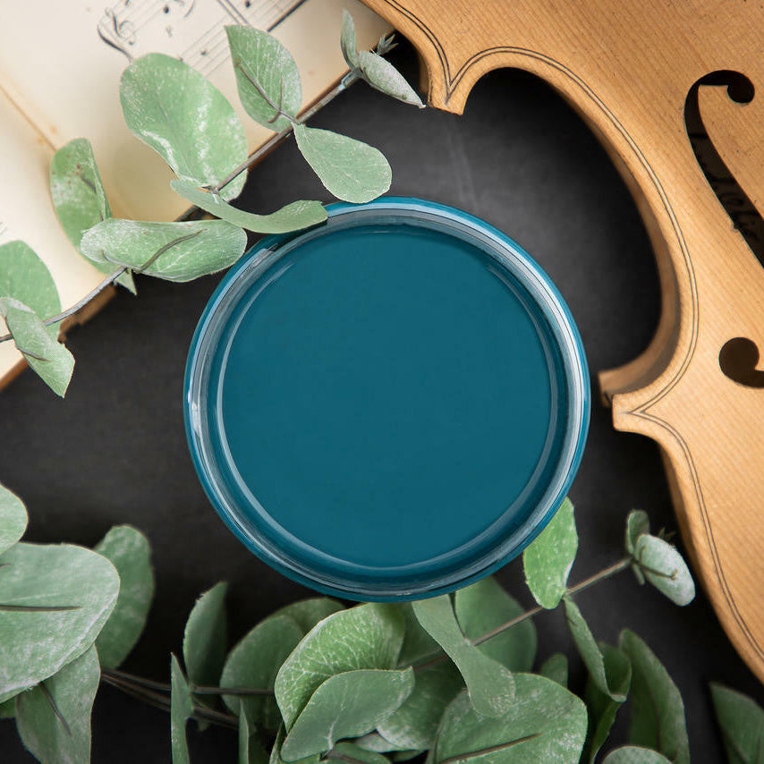 Teal container on a surface with a violin and leaves in the background