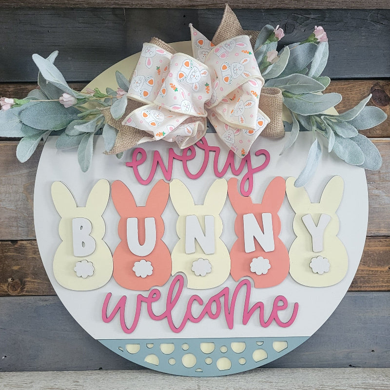 A decorative doorhanger with the text 'Every Bunny Welcome' surrounded by bunny shapes, greenery, and a bow.