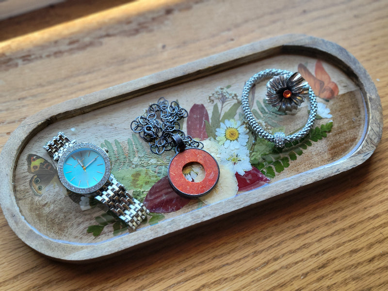 Wooden tray with a watch, necklace, and rings on a wooden surface